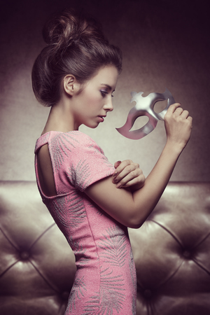 carnival shoot of sexy brunette girl with hair-style and pink dress, taking silver mask in the handの写真素材