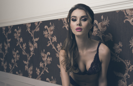 stunning woman with long brown hair and cute make-up posing with elegant lace lingerie and looking in camera with charming expressionの写真素材