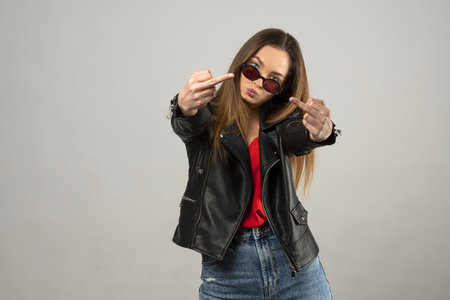 beautiful young lady, in casual dress and sunglasses on white. she is making face and fuck you off with sign handの写真素材