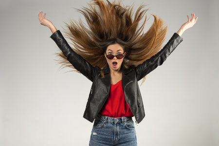 Attractive smiling happy woman making faces isolated on gray studio background. dressed casual with red shirt. she has a lot of hair flying around her headの写真素材