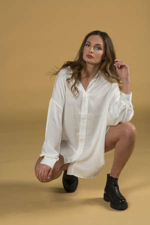 beautiful model, wearing a summer white dreess on beige background looking in camera. she has black bootの写真素材