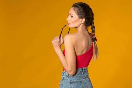 beauty girl showing her back side shoulder, wearing a red top with eye glasses on yellow background. copy spaceの写真素材