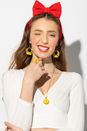 pretty and funny girl , making face closing one eyes , she is in summer dress , and a nice red bow, wearing yellow jewelry with flowerの写真素材
