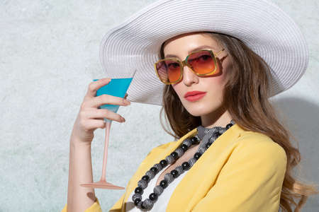pretty young model with yello jacket andhat , drinking a cocktail in relax , in a sunny summer day...