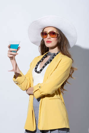 Fashion elegant model , wearing yellow jacket and hat , drinking a cocktail posing on white , with sunglasses in a sunny summer dayの写真素材