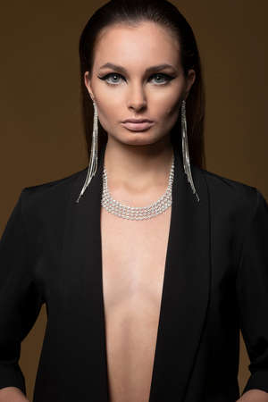 beautiful young woman with diamond jewelery, on dark beige background, she is wearing a black jacket, shining necklace and earrings,の写真素材