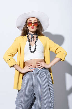 outgoing girl posing under sun day light on white, she wear yellow summer outfit with hat and sunglasses, looking in camera and making duckfaceの写真素材