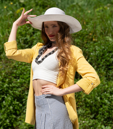pretty woman, in elegant dress going out in a summer day m she is covering her head from sun with a white hat, looking in camera, wearing a jellow jacket and pantsの写真素材