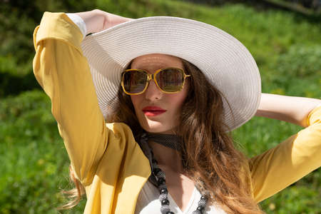 very beautiful young girl, in elegant summer dress, with jellow jacket and hat, she is taking son in a park outside, she has sunglasses, relax and happy conceptの写真素材