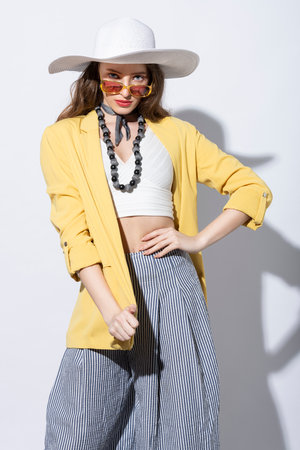 gorgeus young girl in summer outfit, posing in a sun day on white, she dress white hat yellow jacket and sunglasse, she has fashion pantsの写真素材