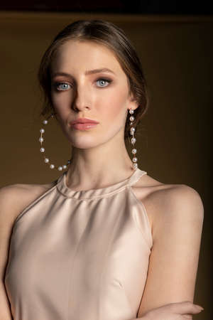 elegant attractive woman with a beige dress, posing very sensual, looking in camera sweetly, she has very big pearls and gold earring.の写真素材