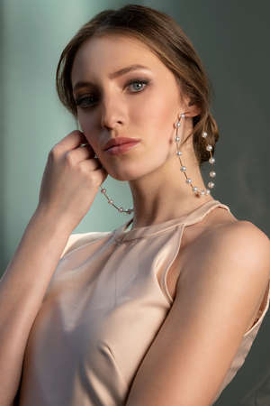 attractive and cute young model in elegant outfit, she is posing in a classic fresh portrait, near a green background, she is looking in camera proudly and touching her face with a handの写真素材