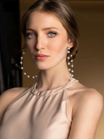 elegant attractive woman with a beige dress, posing very sensual, looking in camera sweetly, she has very big pearls and gold earring.の写真素材