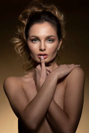 sensual attractive young girl, in a beauty portrait on beige background, she is looking in camera and touching a lip with finger, she has hair style, sexy lookの写真素材