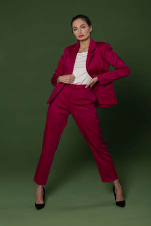 stunning model taking a pose wearing a fuchsia outfit, with jacket and pants, she has high hell posing on greenの写真素材