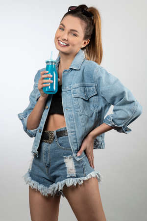 beautiful girl smiling she wear jacket and jeans shorts smiling with a bottle of blue drinkの写真素材