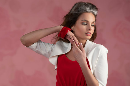 young girl with great hairstyle, posing in a portrait, in fashion style, on pink background, she dress a red shirt and a white jacketの写真素材