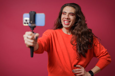 Person creating content with their cell phone on a red background, studio photo, with copy spaceの写真素材