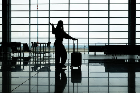 young woman against the light at the airport with travel luggage greeting very happily, copy spaceの写真素材