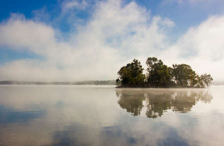 island with reflections and fog on a river one winter morningの写真素材