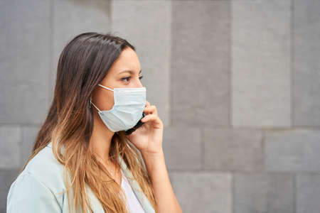 Closeup of a working woman with face mask talking on the phone. On the right there is an empty space...
