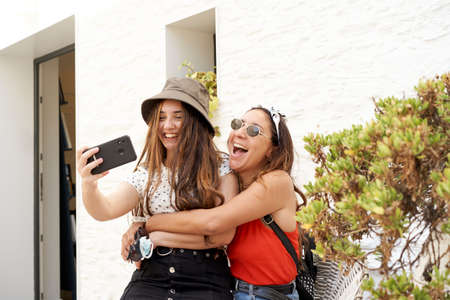 Young sisters taking a selfie. Around there is vegetation and a white wall in the background. Concept of summer, family ...の写真素材