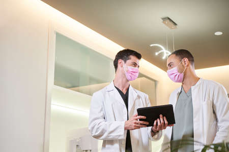 Two doctors in a mask commenting on the results with a tablet in hand. Gynecological, dental or aesthetic clinic. Medical concept.の写真素材