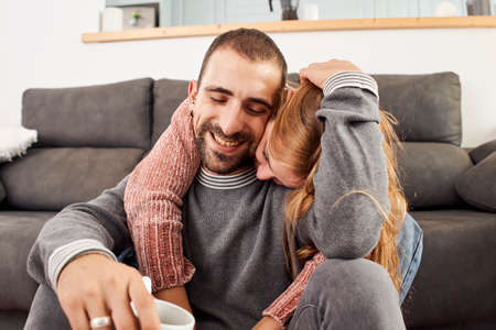 Happy young couple relaxing talking holding cups of coffee on the couch together in the living room.の写真素材