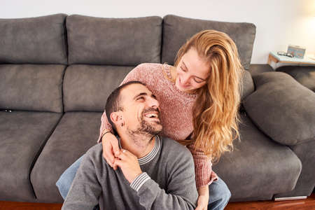 Happy young couple relaxing talking holding cups of coffee on the couch together in the living room.