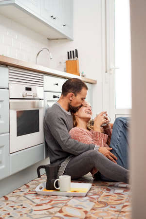 Top view of a beautiful young couple drinking coffee while sitting on the kitchen floor at home.の写真素材