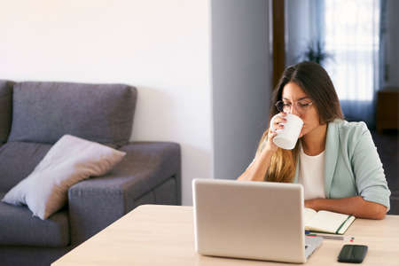 Woman working at home with laptop and drinking coffee.の写真素材