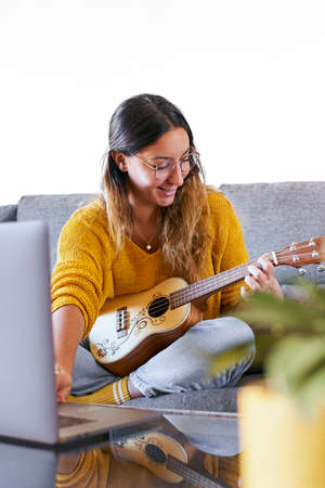 Woman learning to play ukulele online from her laptop during covid quarantine.