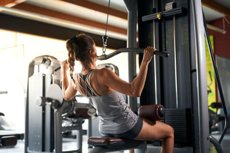 View from behind of beautiful young woman in sports shorts and a gray tank top engaged in fitness in...