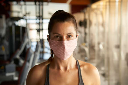Close up of young woman with sportswear with face mask looking at camera in gym.の写真素材