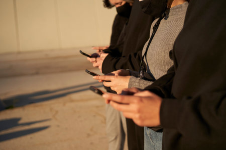 Hands of a group of friends using a smart phone. They are dressed in black and gray, without any...