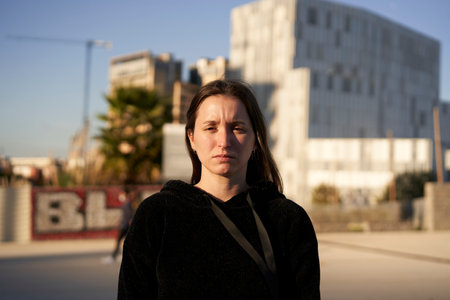 Looking to the camera. Portrait of a serious Hispanic young woman while standing in a city.の写真素材