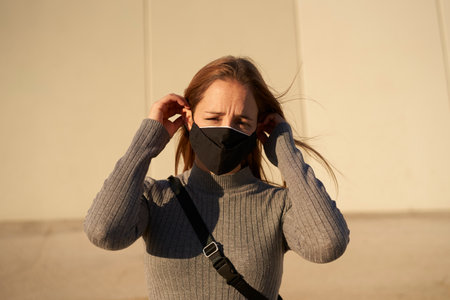 Looking to the camera. Portrait of a smiling Hispanic young girl putting on a mask due to the...