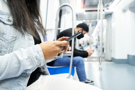 Close up of a woman's hands and a in background sitting in the subway car using the smartphone and...