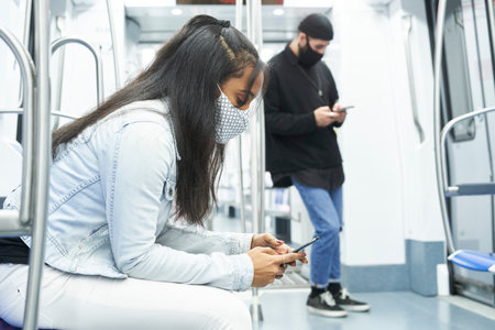 An African American girl and a Caucasian boy using the smartphone in the subway car. Young people in public transport abducted by technology.の写真素材