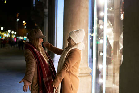 Reconnect of 2 young women, happy and excited to see each other again, embrace each other with enthusiasm. They are in a city at night and wear winter clothes. Together againの写真素材