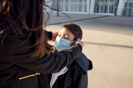Mother puts a safety mask on her child's face. Child going to play in the park with covid-19 precautions. Medical mask to prevent coronavirus. Coronavirus quarantine, new normal.の写真素材
