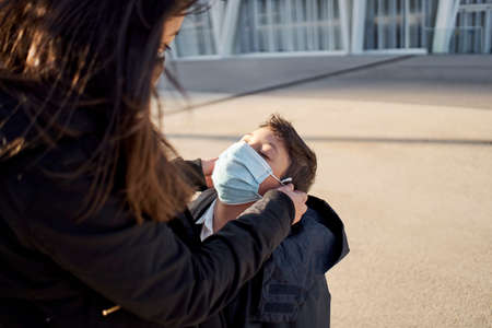 Mother puts a safety mask on her child's face. Child going to play in the park with covid-19...