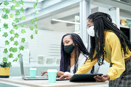 African American female coworkers talk about work together share ideas about digital marketing strategy at office meeting.の写真素材