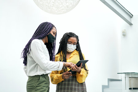 Two focused young businesswoman talking over a digital tablet while having a meeting together in a modern office.の写真素材