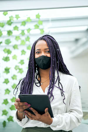 Vertical shot of portrait of a businesswoman looking camera in the office using a tablet. She turns...