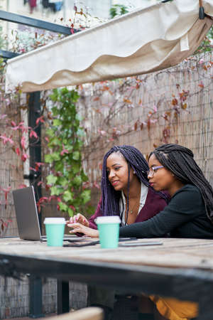 Vertical shot of two young latin women using a laptop outdoors.の写真素材