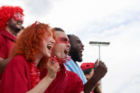 Group of people of different races follow the soccer match in the stands. Men and women celebrating...