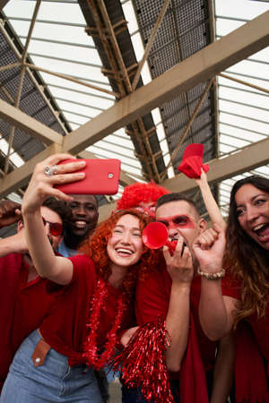 Vertical photo of a group of people taking a smiling selfie while cheering for their sports team...