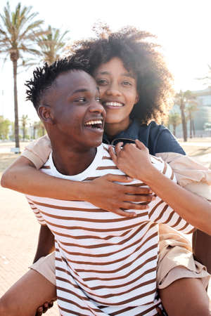 Vertical portrait of a young African-American couple in love. The girlfriend piggybacking the boyfriend.の写真素材