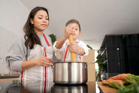 In the kitchen: A single-parent family cooking pasta together. Mother and son putting pasta to boil. Children helping parents. Healthy eating.の写真素材